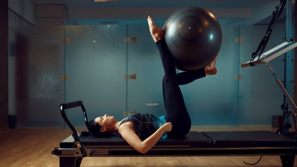 lady doing pilates reformer exercise with the swiss ball on the legs